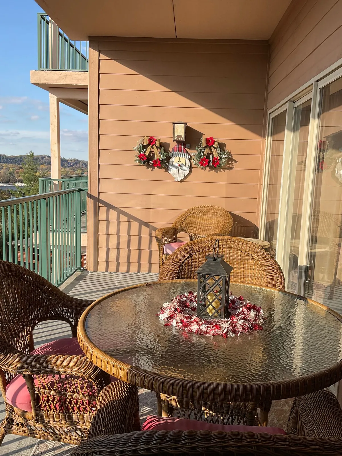 A cozy exterior balcony scene featuring wicker chairs and a glass table set for relaxation. The balcony is adorned with decorative lanterns and festive holiday wreaths, providing a warm, inviting atmosphere. The setup is oriented to maximize enjoyment of the surrounding views, ideal for morning coffee or an evening drink.