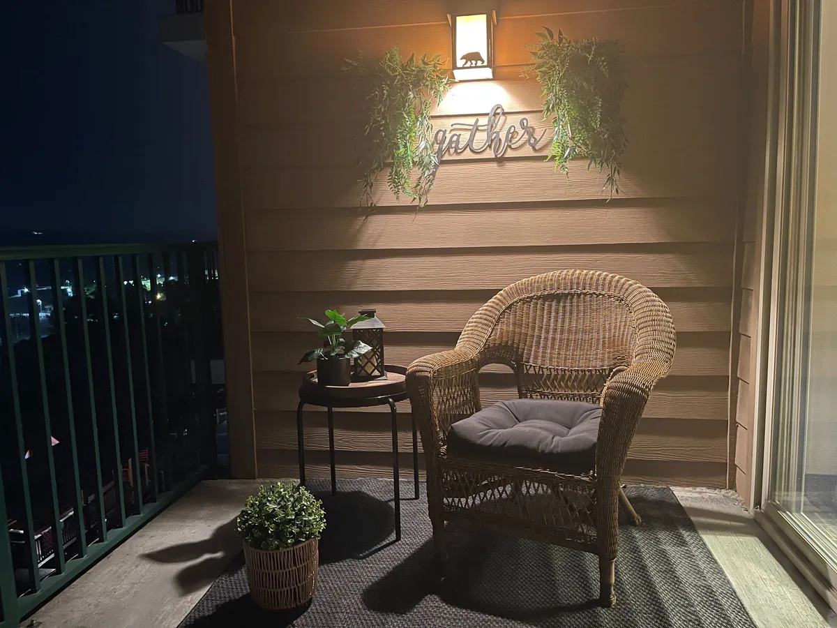 This exterior image features a cozy wicker chair and small table set on a porch, accented by a decorative sign and plants. The lighting suggests a welcoming atmosphere ideal for relaxing or sharing stories outdoors, with hints of nighttime comfort under the porch light.