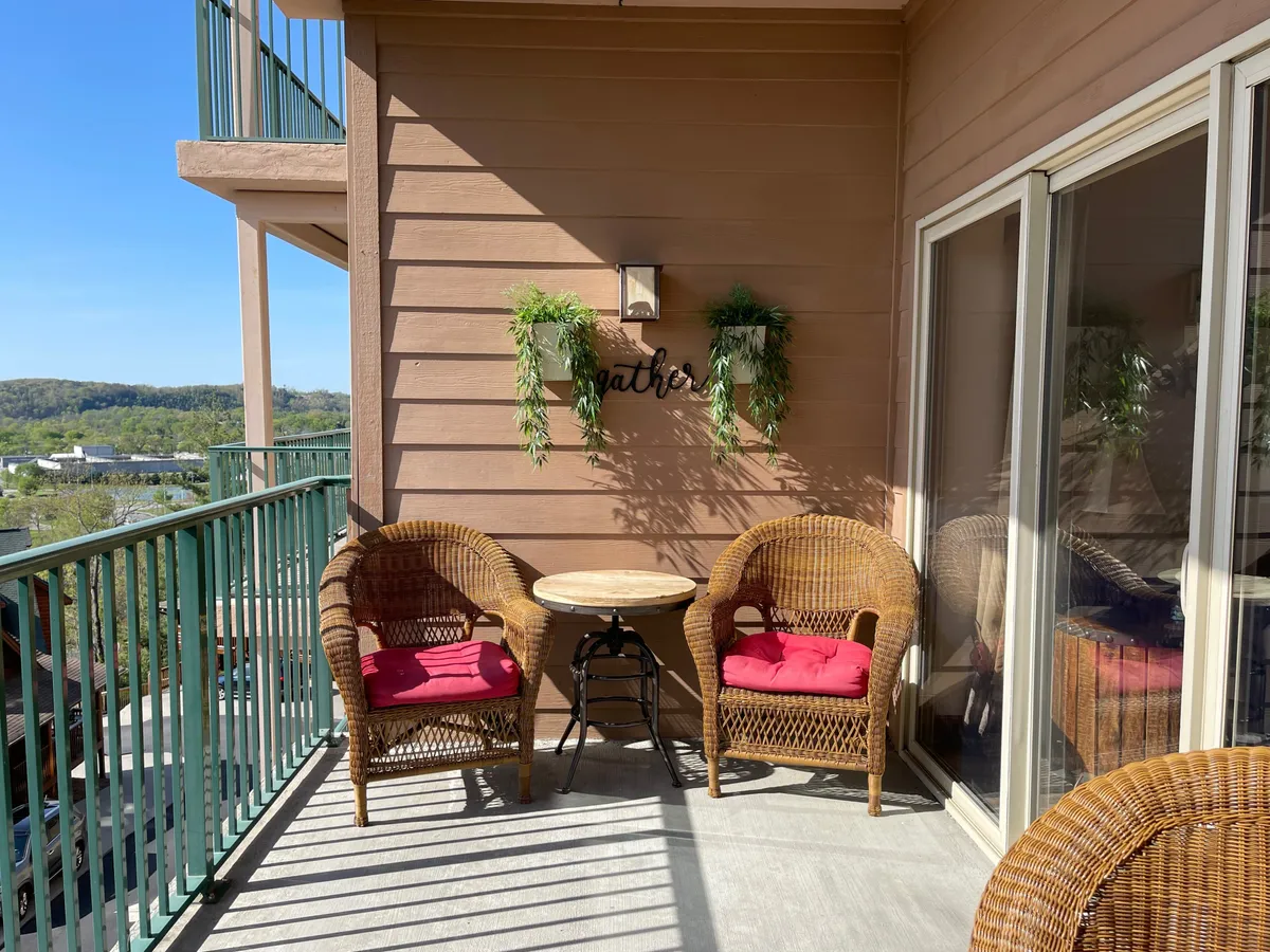 An exterior image featuring comfortable wicker chairs, a small round table, and hanging plants set against a welcoming porch. The space is designed for casual conversation, morning coffee, or evening chats, embodying hospitality and togetherness.