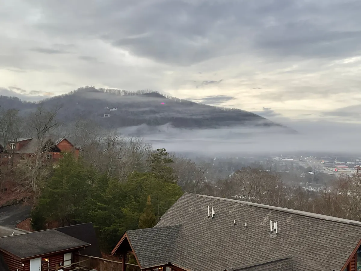 A panoramic view of a Smoky Mountain range, with layers of fog gently hugging the valley below and a golden sunset casting a romantic glow over the landscape. The tranquil atmosphere invites guests to reflect or enjoy the scenery together.