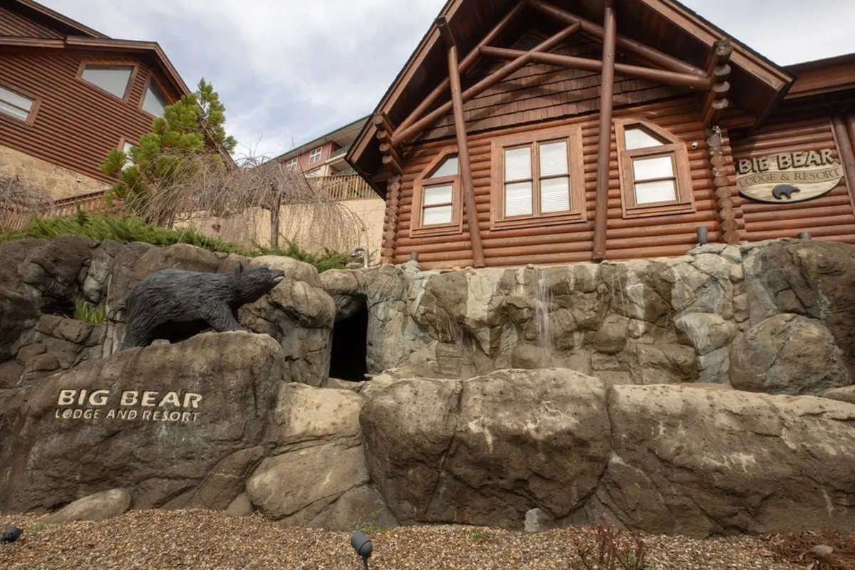 The rustic log cabin exterior with a charming bear sculpture and rocky landscaping, nestled in natural surroundings. The welcoming mood evokes the comfort and seclusion of a mountain hideaway.