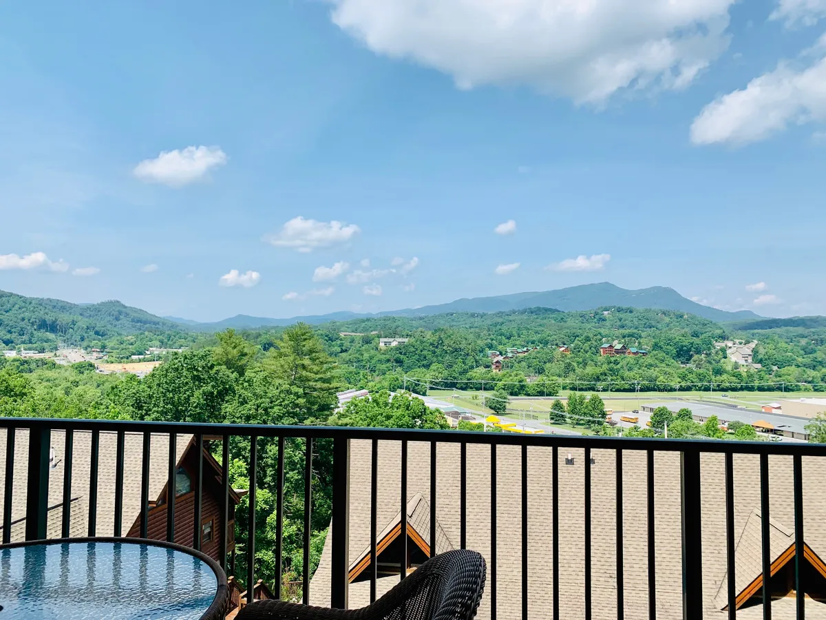 A stunning, peaceful view of the Smoky Mountain range, with lush green trees and a clear blue sky. The vantage point suggests the view is enjoyed from a balcony or similar elevated position, echoing the promise of mountain vistas right outside.
