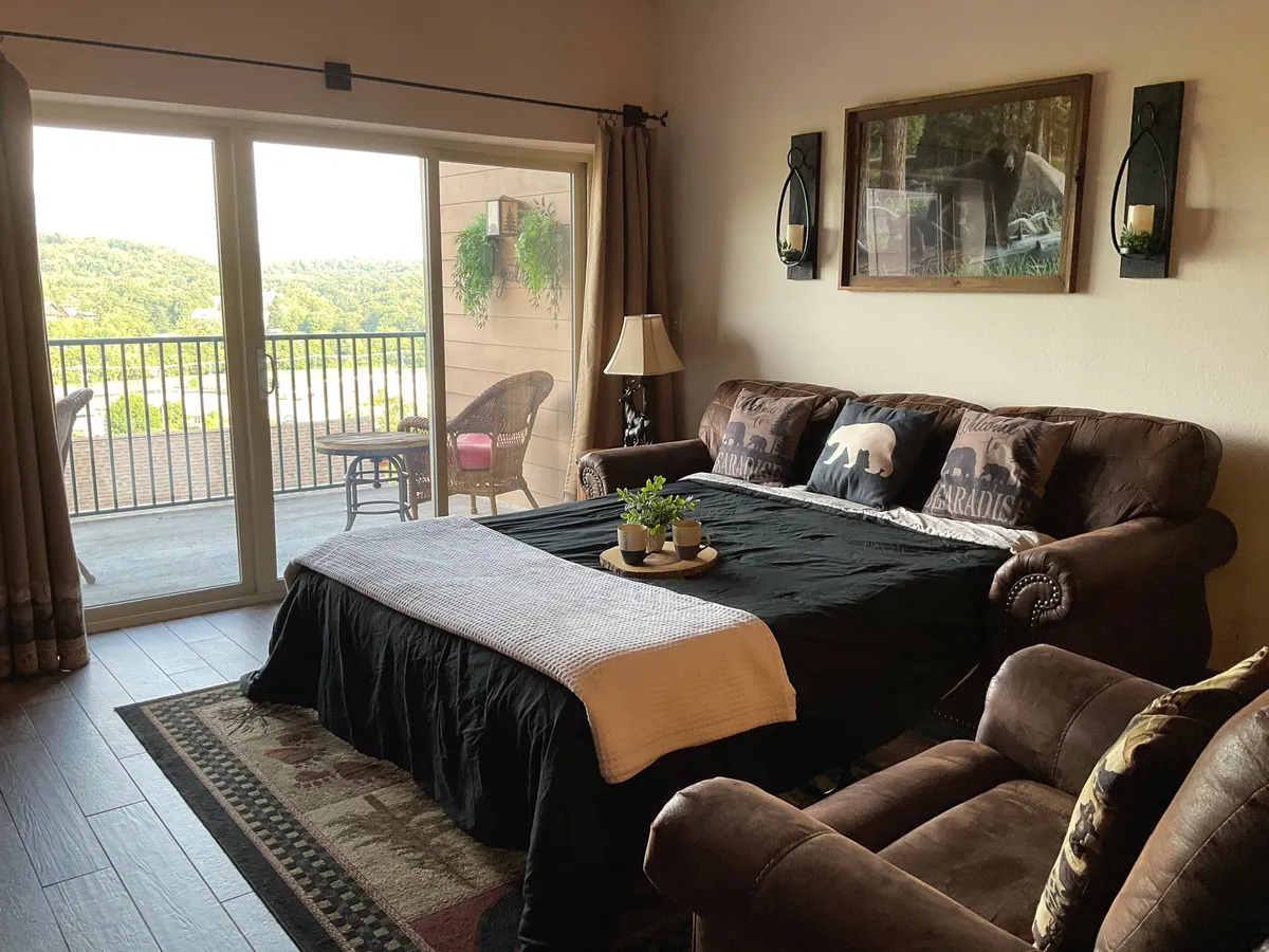 This image showcases a comfortable living area featuring a sofa with decorative pillows, a coffee table adorned with plants, and large sliding doors opening to a balcony. Natural light fills the space, and the balcony provides a seamless transition to the outdoors, suggesting opportunities for relaxation with mountain views.