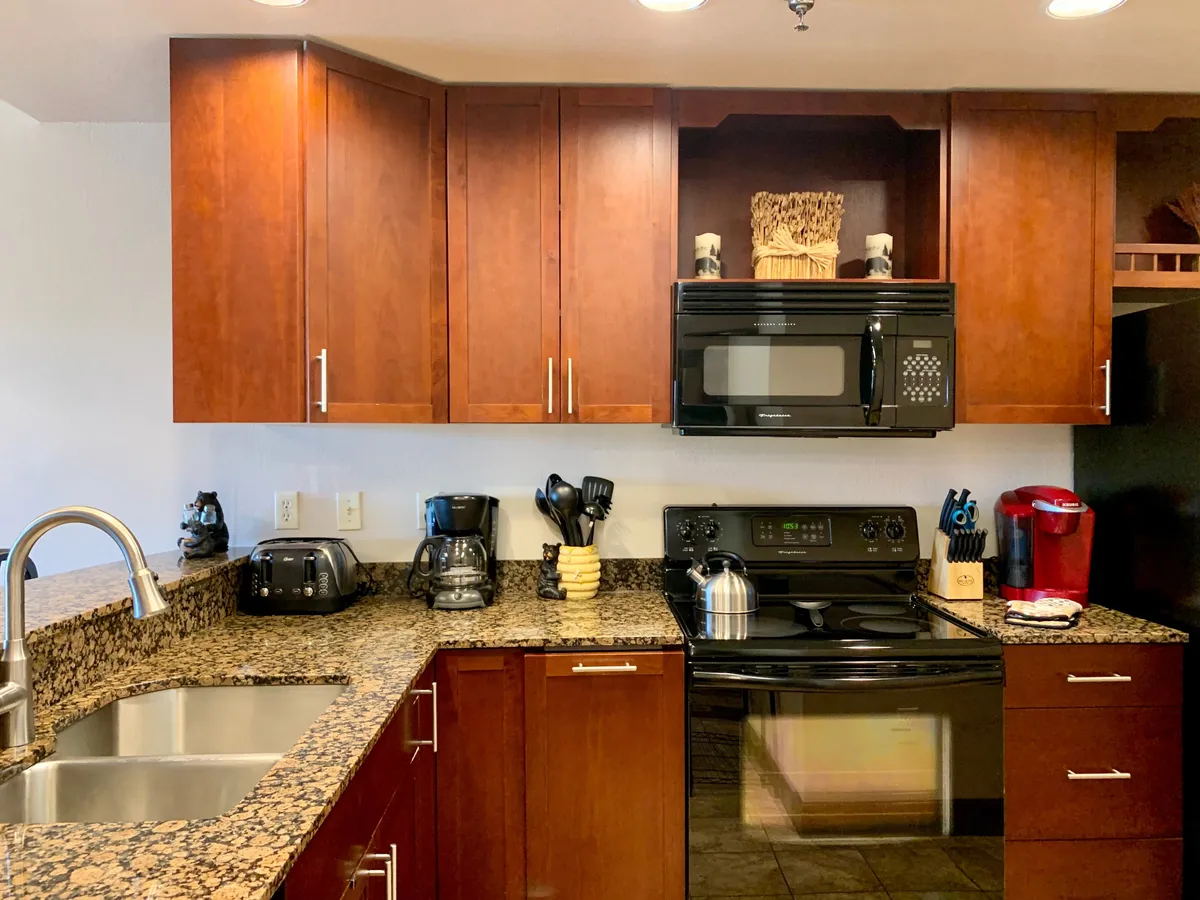 This image reveals a kitchen with granite countertops, modern appliances, and wooden cabinets. Kitchen utensils are neatly arranged, and the space is bathed in warm, inviting light. The setup encourages both cooking and socializing, with a clear view of the counter and prep area.